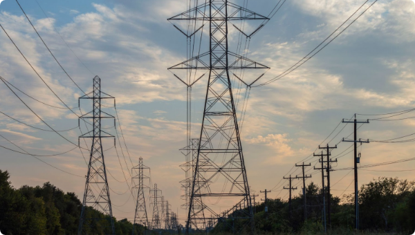 Row of transmission towers and utility poles carrying power lines at dusk